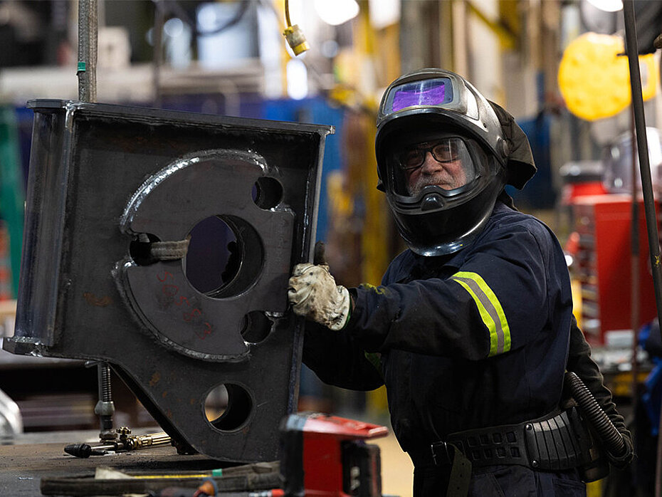 Employee wearing full protective equipment handling an industrial component inside a manufacturing facility.